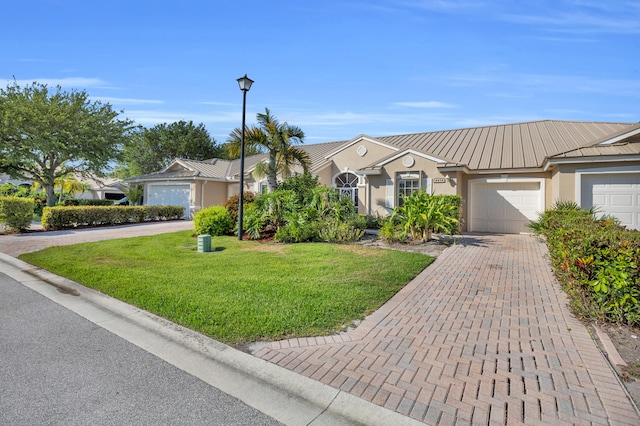 ranch-style house with stucco siding, decorative driveway, a front yard, a garage, and metal roof