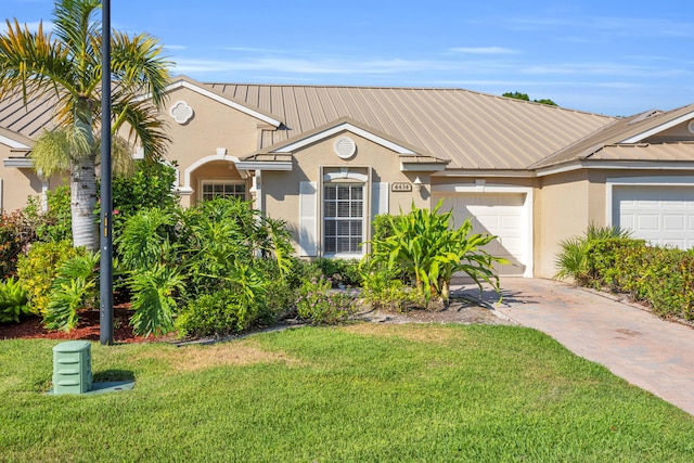 view of front of home with stucco siding, a garage, a front yard, metal roof, and driveway
