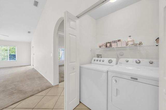 laundry area featuring washer and clothes dryer, arched walkways, light carpet, and light tile patterned flooring