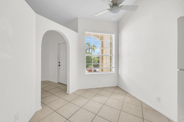 unfurnished room with arched walkways, a ceiling fan, light tile patterned floors, and baseboards