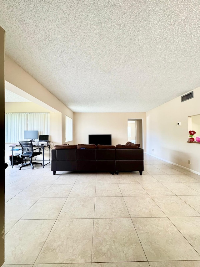 living area featuring a textured ceiling, light tile patterned flooring, and a desk