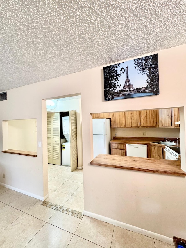 unfurnished living room with light tile patterned floors, a sink, a textured ceiling, washer / dryer, and baseboards