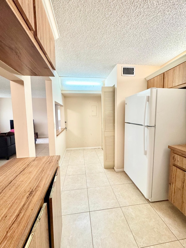 kitchen featuring freestanding refrigerator, light tile patterned flooring, light countertops, and a textured ceiling
