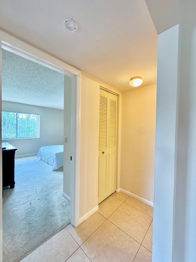 hallway with light tile patterned floors, baseboards, and light carpet