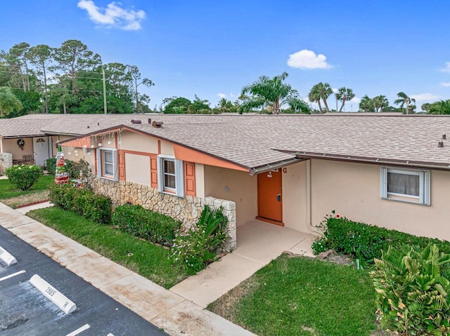 ranch-style home with a shingled roof, stucco siding, stone siding, and uncovered parking