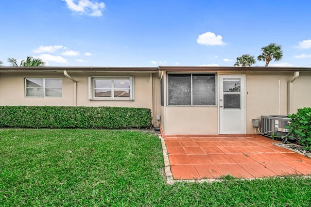 rear view of property featuring stucco siding, central air condition unit, a lawn, and a patio