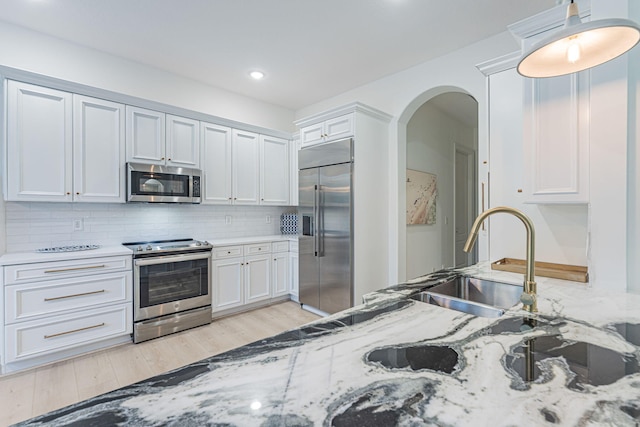 2068 Wightman Dr, Wellington, FL 33414 - kitchen featuring appliances with stainless steel finishes, decorative backsplash, arched walkways, light wood-style floors, and light stone countertops