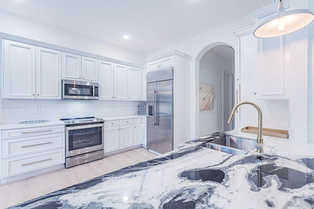 2068 Wightman Dr, Wellington, FL 33414 - kitchen featuring stainless steel appliances, arched walkways, tasteful backsplash, white cabinetry, and light wood-type flooring