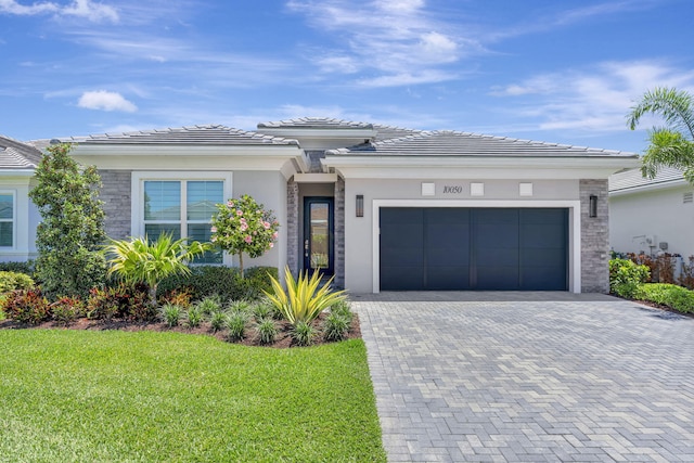 prairie-style home with an attached garage, driveway, a front yard, a tiled roof, and stucco siding