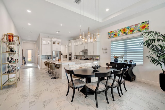 dining room featuring recessed lighting, a high ceiling, light marble finish flooring, and baseboards