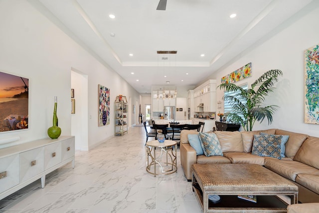 living area featuring recessed lighting, a raised ceiling, baseboards, light marble finish floors, and a ceiling fan