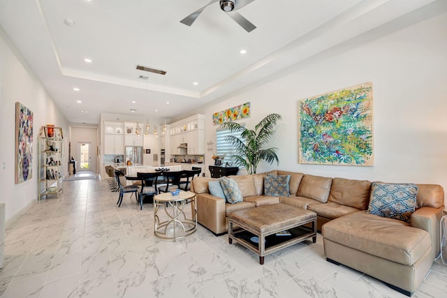 living room with recessed lighting, ceiling fan, a raised ceiling, baseboards, and light marble finish floors