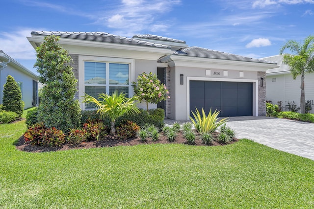 prairie-style home with a garage, a tile roof, a front lawn, decorative driveway, and stucco siding