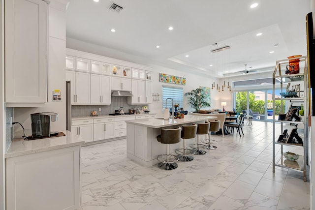 kitchen featuring light marble finish floors, recessed lighting, gas stovetop, under cabinet range hood, and white cabinets