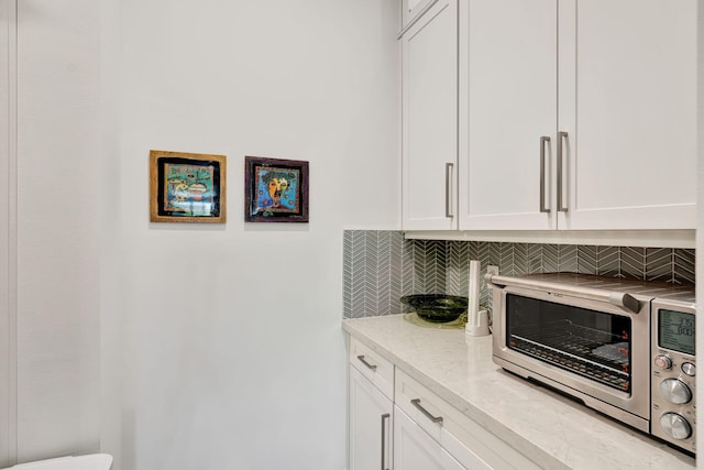 kitchen with decorative backsplash, white cabinetry, and light stone counters