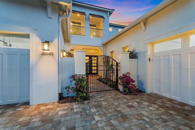 20049 SE Bridgewater Dr, Jupiter, FL 33458 - exterior entry at dusk featuring a gate, stucco siding, a balcony, and a garage