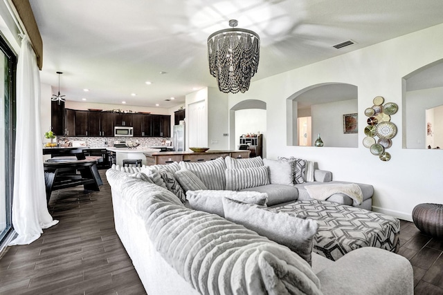living area with arched walkways, a chandelier, dark wood-type flooring, baseboards, and recessed lighting