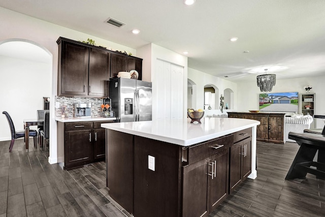 kitchen with stainless steel refrigerator with ice dispenser, arched walkways, light countertops, dark wood-type flooring, and recessed lighting