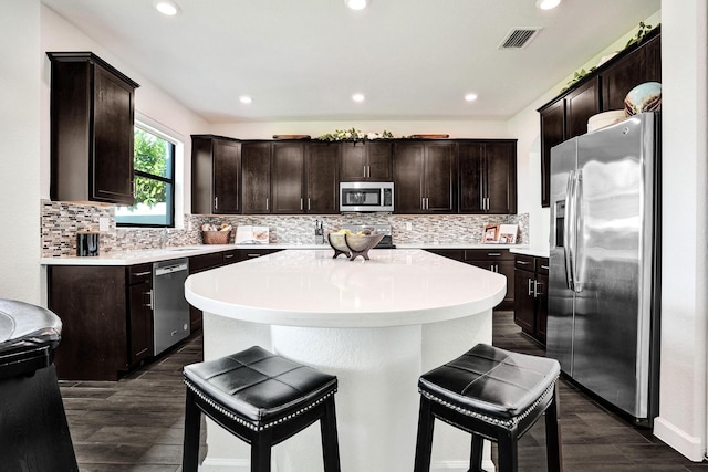 kitchen featuring appliances with stainless steel finishes, a kitchen bar, a kitchen island, dark brown cabinetry, and recessed lighting