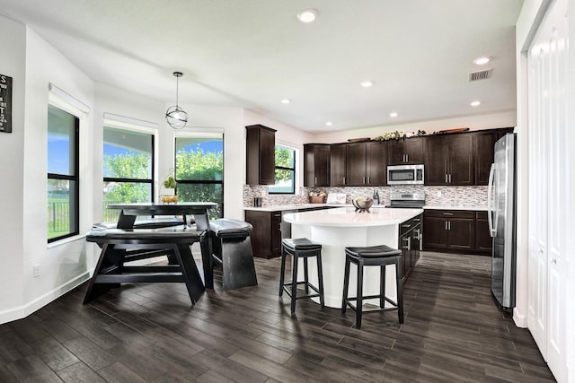 kitchen featuring stainless steel appliances, a kitchen island, dark brown cabinets, backsplash, and a breakfast bar area