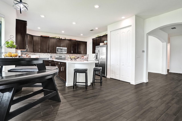 kitchen with appliances with stainless steel finishes, dark brown cabinetry, dark wood-style flooring, arched walkways, and recessed lighting