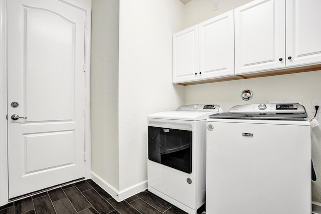 clothes washing area featuring washing machine and dryer, cabinet space, wood tiled floors, and baseboards