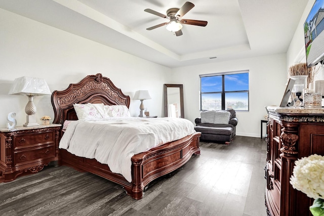 bedroom featuring a raised ceiling, dark wood finished floors, ceiling fan, and baseboards