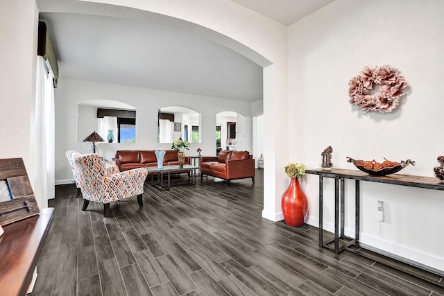 living area featuring arched walkways, dark wood finished floors, and baseboards