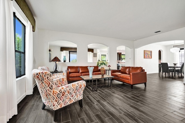 living area with dark wood-type flooring, arched walkways, and baseboards