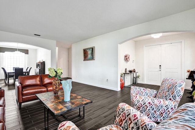 living area featuring arched walkways, dark wood-type flooring, baseboards, and a chandelier