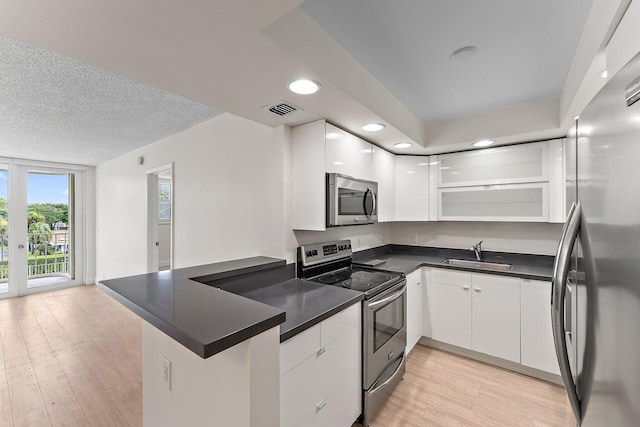 kitchen featuring stainless steel appliances, a sink, a peninsula, dark countertops, and white cabinetry