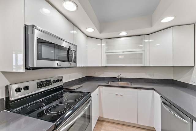 kitchen featuring stainless steel appliances, a sink, white cabinets, dark countertops, and modern cabinets