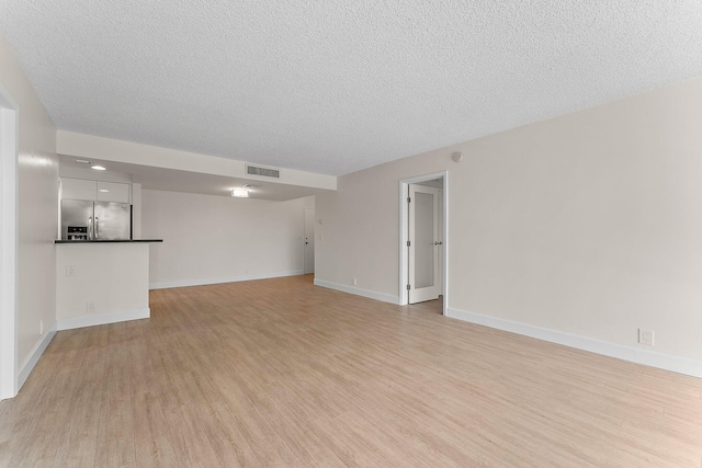 unfurnished living room with light wood finished floors, a textured ceiling, and baseboards