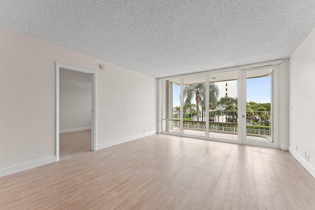 spare room with expansive windows, plenty of natural light, a textured ceiling, light wood-style flooring, and baseboards