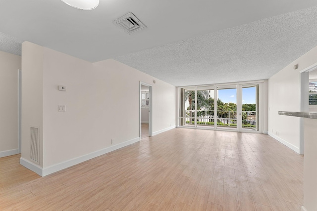 unfurnished living room featuring a textured ceiling, healthy amount of natural light, baseboards, light wood finished floors, and floor to ceiling windows