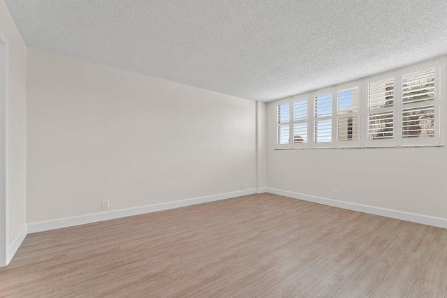 spare room with a textured ceiling, light wood-style flooring, and baseboards