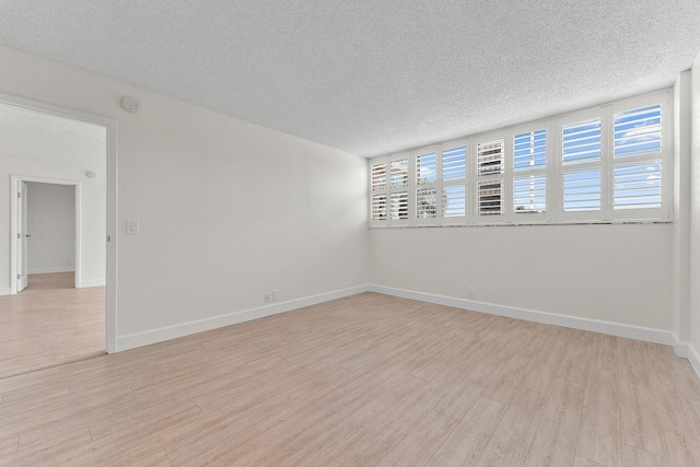 unfurnished room with a textured ceiling, wood finished floors, baseboards, and a smoke detector