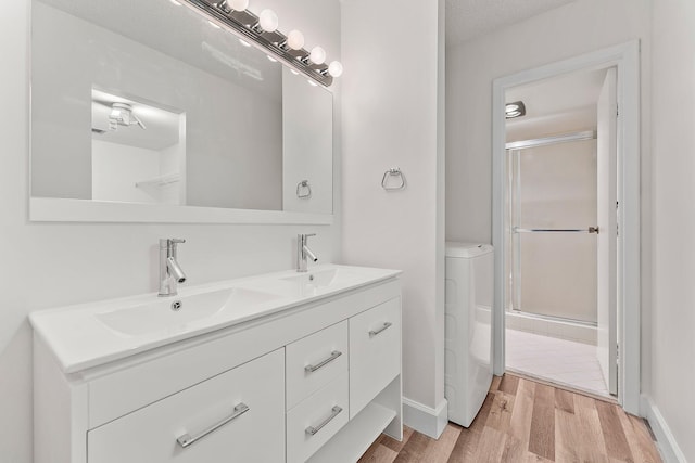 bathroom featuring wood finished floors, double vanity, a shower with shower door, and baseboards