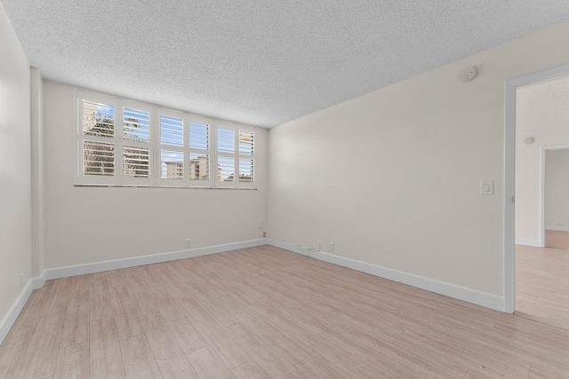 spare room with a textured ceiling, light wood-style floors, a smoke detector, and baseboards