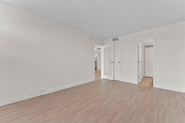 unfurnished room featuring light wood-style flooring, baseboards, and a textured ceiling