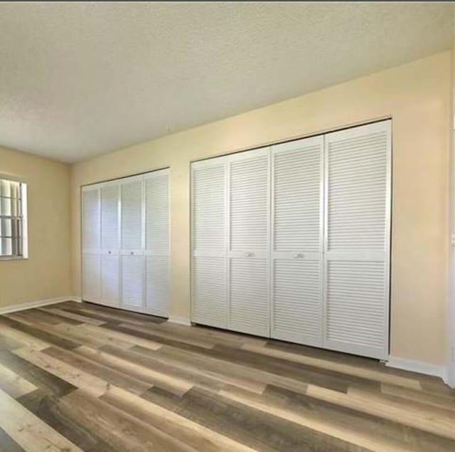 4155 NW 90th Ave Unit 106, Coral Springs, FL 33065 - unfurnished bedroom with multiple closets, baseboards, wood finished floors, and a textured ceiling