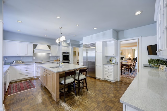 218 El Brillo Way, Palm Beach, FL 33480 - kitchen with stainless steel built in fridge, custom range hood, a sink, tasteful backsplash, and an island with sink