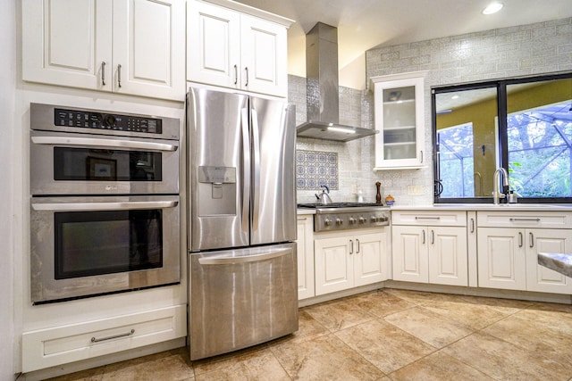 kitchen with appliances with stainless steel finishes, wall chimney exhaust hood, decorative backsplash, white cabinets, and a sink