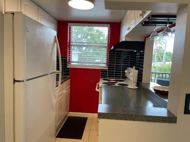 111 SE 1st St Unit 7, Boynton Beach, FL 33435 - kitchen with white appliances, dark countertops, light tile patterned floors, white cabinetry, and under cabinet range hood