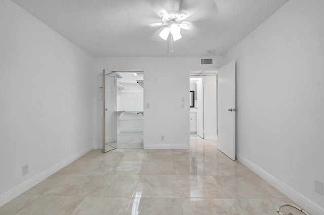 unfurnished bedroom with a walk in closet, a closet, a ceiling fan, and baseboards