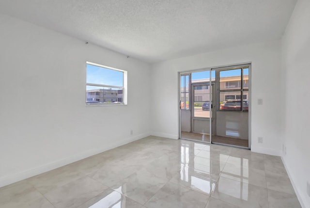 empty room featuring plenty of natural light, a textured ceiling, and baseboards