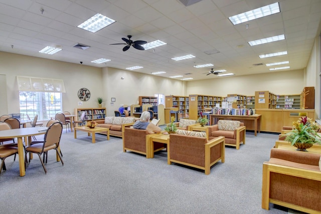 living area featuring a ceiling fan, light carpet, and a drop ceiling