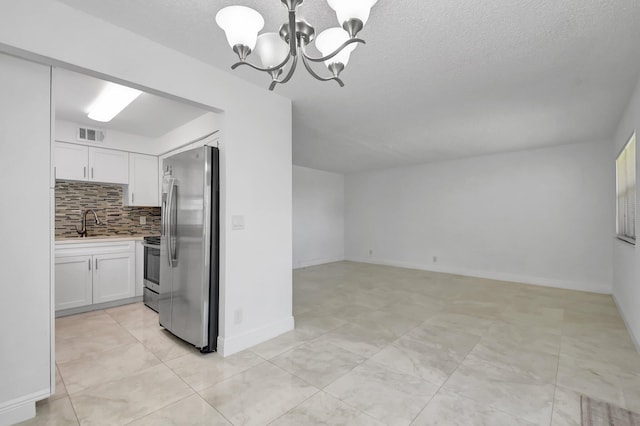 kitchen featuring stainless steel appliances, a chandelier, white cabinetry, decorative backsplash, and a textured ceiling