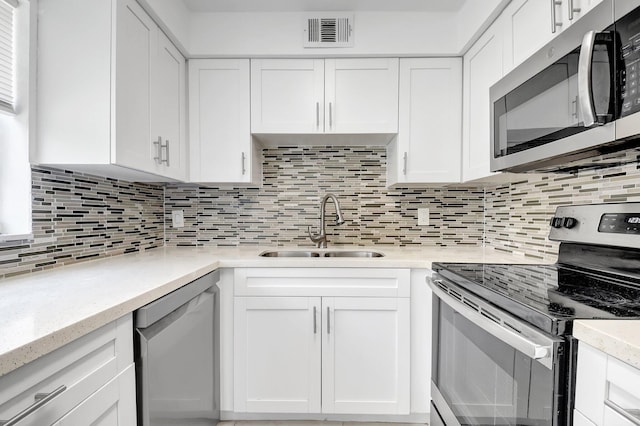 kitchen with appliances with stainless steel finishes, a sink, white cabinetry, decorative backsplash, and light stone countertops