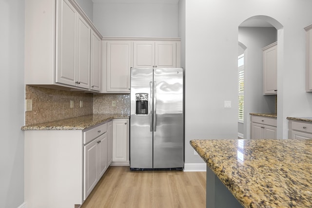 17009 SW Sapri Way, Port Saint Lucie, FL 34986 - kitchen featuring stainless steel fridge with ice dispenser, light wood-type flooring, arched walkways, decorative backsplash, and light stone counters